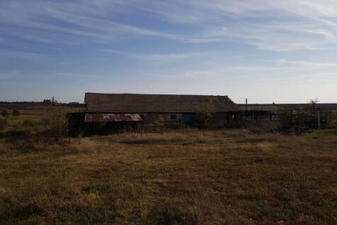 Wide view of the farm building with tiled roof and metal fencing, set in open grassy land under a partly cloudy sky.