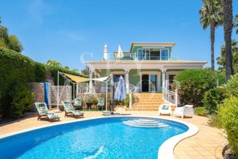 Luxury coastal estate in Carvoeiro, Algarve, featuring a large private swimming pool, sun loungers, and expansive sun-drenched terraces leading to a traditional Algarvian style villa.