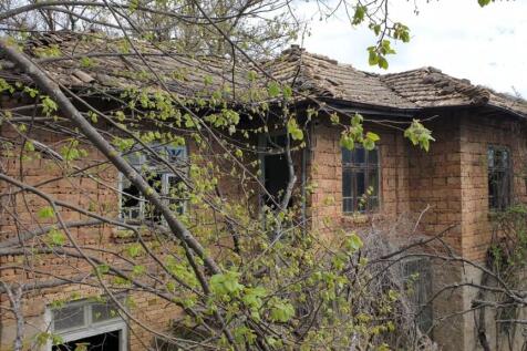 Exterior view of an old brick house with a tiled roof surrounded by leafing trees