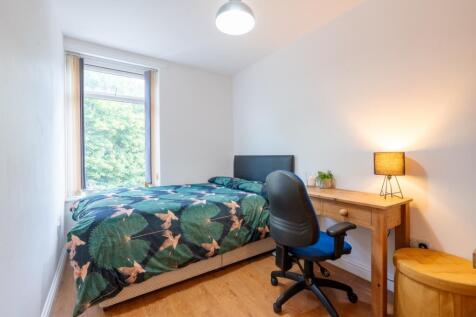 A well-lit, cozy single bedroom featuring a bed...