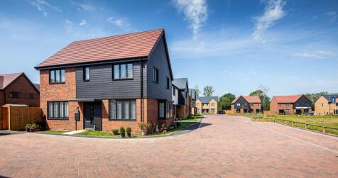A modern brick and dark-paneled house with a red-tiled roof sits in the foreground on a paved drivew