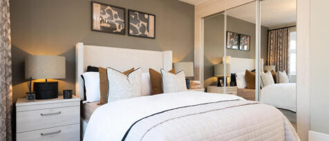 Modern bedroom with a white bed, beige and grey cushions, mirrored wardrobe, and framed abstract art