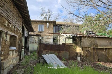 The rear yard area with old outbuildings made of wood and metal sheets, and the back of the two-storey house with windows and doors.
