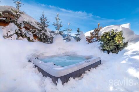 A hot tub is surrounded by snow and small evergree