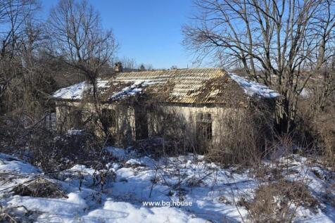 An old house with a partially damaged roof and snow on the ground, surrounded by bare trees in winter.