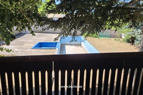 View of an empty swimming pool and garden area seen through the wooden balcony railing.
