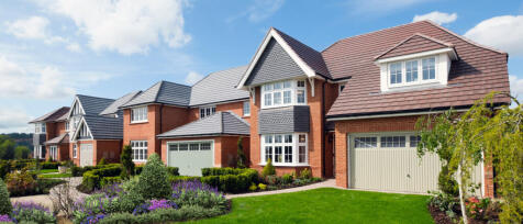 Modern red-brick houses with grey and red tiled roofs, surrounded by colourful gardens and green law