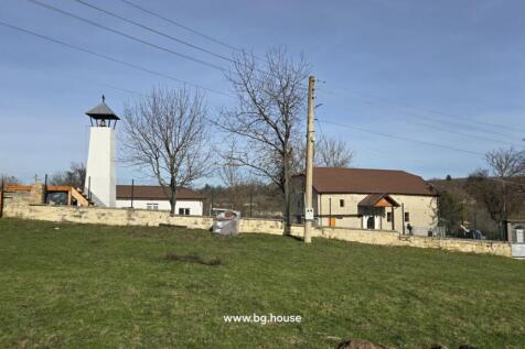 View of a white bell tower and a fenced house situated on a grassy hill with trees around.