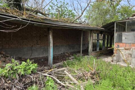 Brick outbuilding with wooden supports and glass porch adjacent to the house, surrounded by overgrown vegetation