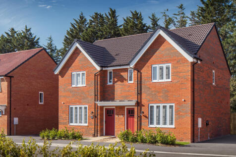 A pair of modern brick semi-detached houses with red doors and white-framed windows stand in the for