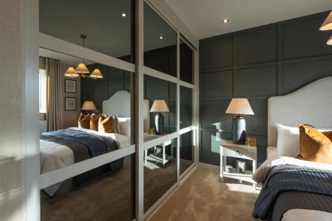 A bedroom with a mirrored wardrobe reflecting a bed in the foreground and a dark paneled wall behind