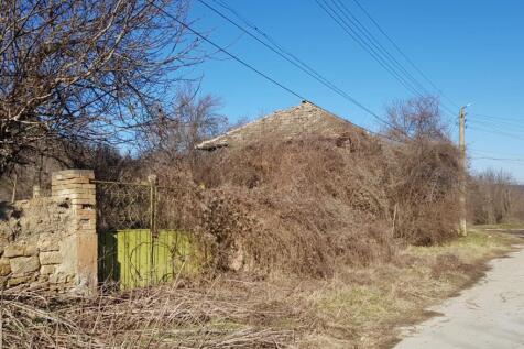 Side view of an old house with a green metal gate and dry vegetation around