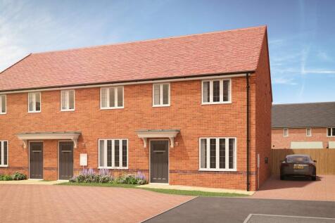 A row of modern brick townhouses with red tile roofs stands on a paved driveway