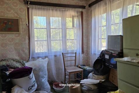 Interior view of a cluttered room featuring floral curtains, a chair, and assorted household items scattered around.