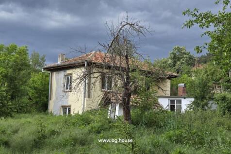 Exterior view of a two-storey yellow house with a tiled roof and surrounding greenery in Koprivets village.