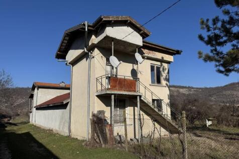 Side perspective showing a two-story rural house with an external concrete staircase and satellite dishes mounted on the wall.