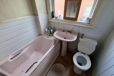 A compact bathroom featuring a pastel pink bath...