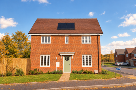 A two-story red brick house with a green front door and solar panels sits behind a green lawn and wo