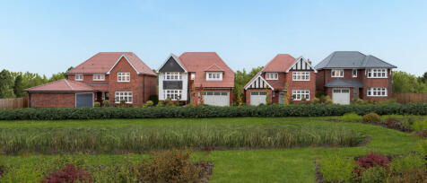 A row of modern detached houses with brick exteriors and pitched roofs, surrounded by greenery and a