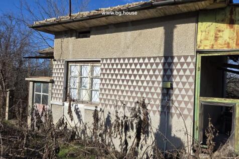 Close-up side view of the house showing patterned exterior walls, windows with metal grilles, and a rusty metal frame structure.