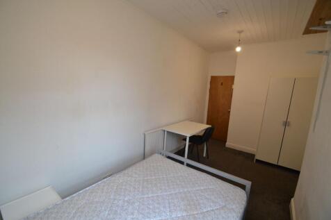 A small, simple room featuring a plain bed, a w...