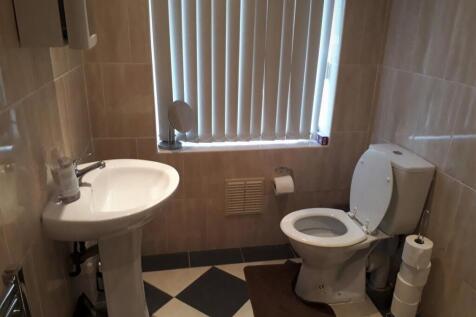 Clean tiled toilet with pedestal sink and windo...
