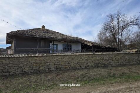 View of a traditional Bulgarian house featuring a tiled roof and a stone perimeter wall in Slavyanovo village.