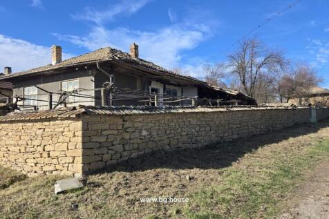 Stone wall enclosing a traditional Bulgarian house with tiled roof and chimney under clear blue sky