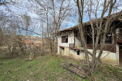 Side perspective of the old house showing white plaster walls, wooden balcony, and surrounding bare trees.