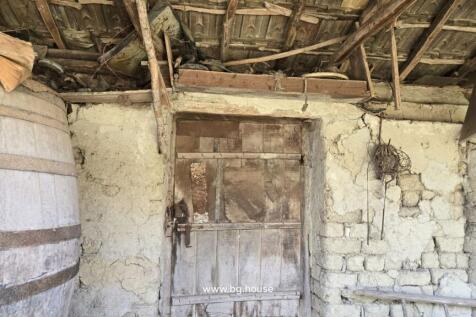 Close-up view of a rustic stone wall featuring a wooden door and a large barrel under a wooden roof structure.