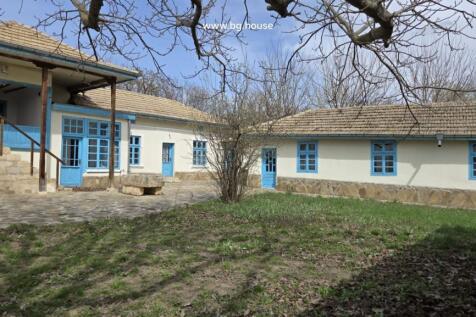 Stone paved courtyard with grass patches and traditional house walls featuring blue framed windows and doors.