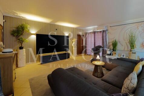 Angled view of a bright living room featuring a vertical wood slat media wall, large TV, comfortable dark sofas, and sliding doors to a private sun terrace.
