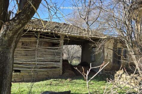 Hay stored in a wooden structure beside a stone building surrounded by trees