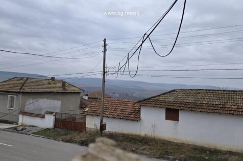 View from a window showing rooftops of village houses, power lines, and hills in the distance.