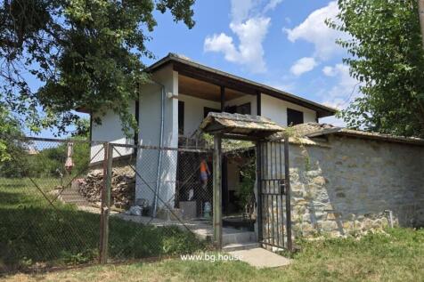 Front view of a traditional Bulgarian house with a gated entrance and stone wall under a blue sky