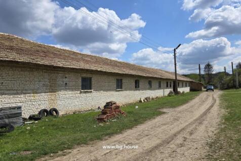 Exterior view of a long white brick farm building with a tiled roof along a dirt road in Osikovo village
