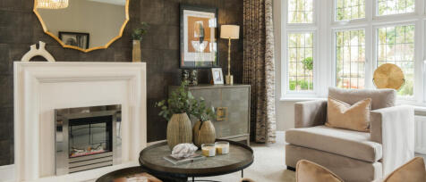 A cosy living room with a white fireplace, beige armchair, decorative vases, framed artwork, and lar
