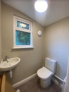 A clean and well-lit single toilet with a sink ...