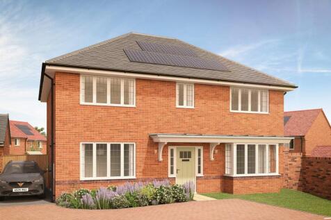 A modern brick house with solar panels on the roof sits behind a colorful flowerbed and a paved driv