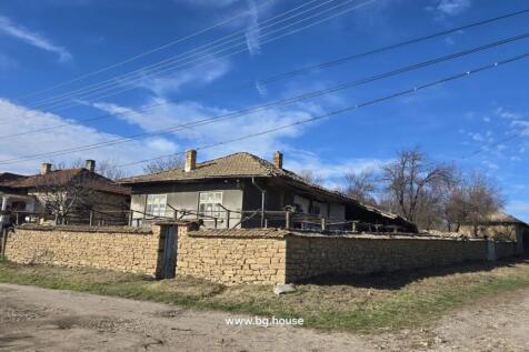 Corner perspective showing stone wall surrounding a Bulgarian house with tiled roof and dirt road