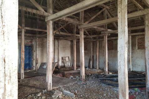 Interior of a farm building showing wooden support beams, debris on the floor, and a blue door in the background.