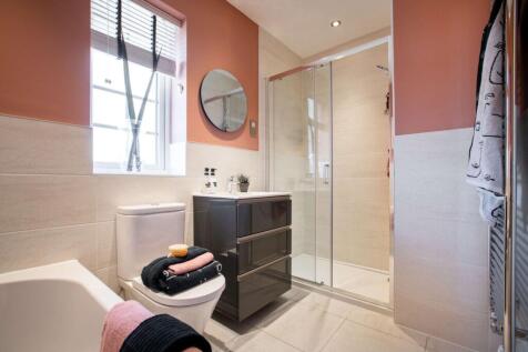 A modern bathroom features a toilet with folded towels in the foreground and a glass-enclosed shower