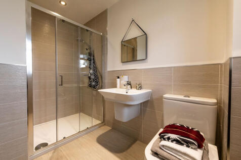 A modern bathroom features a glass-enclosed shower in the foreground and a toilet with folded towels