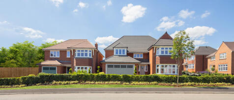 A row of modern detached houses with brick exteriors and well-maintained gardens under a blue sky wi