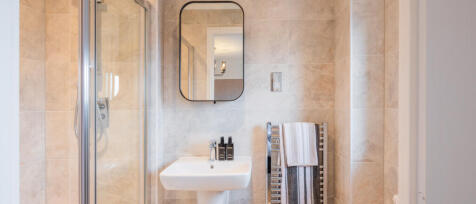 Modern bathroom with beige tiled walls, a small white sink, a wall-mounted mirror, and a heated towe