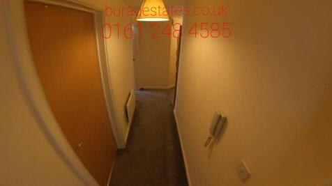 Narrow carpeted hallway with neutral walls, ove...