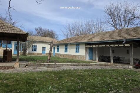 Exterior view of a traditional Bulgarian house with blue doors and windows and a tiled roof surrounded by leafless trees.