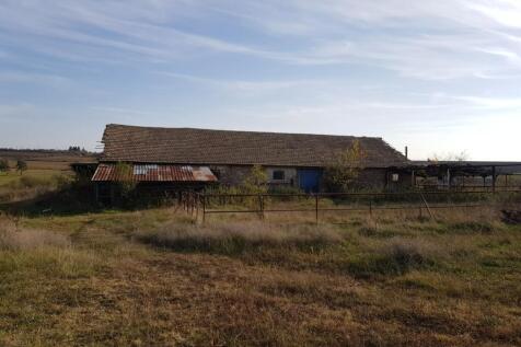 View of the long farm building with a tiled roof and metal fencing in front, surrounded by dry grass and open countryside.