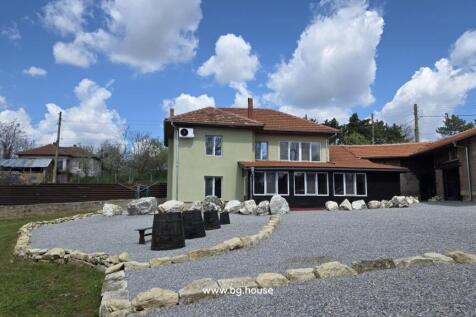 Two-storey house with green exterior walls and red tiled roof surrounded by gravel yard and stone borders