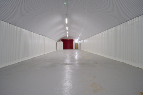 An empty arch with white lining, facing the front electric roller shutter entrance, which is closed. There is a WC cubicle at the front of the arch.